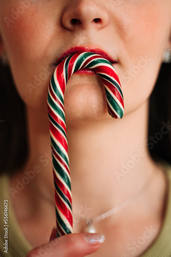 A beautiful woman holds a Christmas candy lollipop near her lips. New Year, warm and cozy atmosphere.