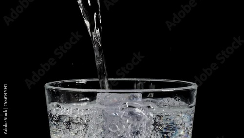 glass with ice filling with tonic until it overflows in super slow motion on a black background