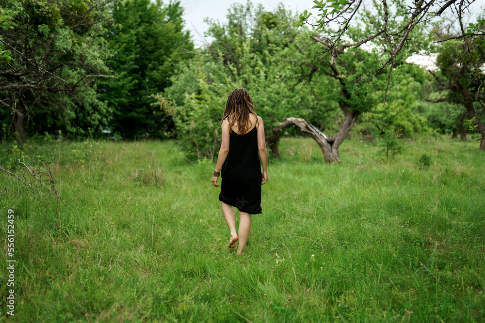 Girl with dreadlocks in a black dress walks in the garden