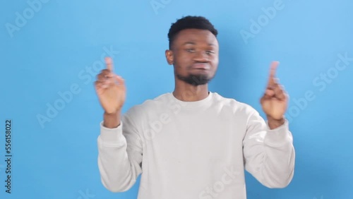 A young African American he gestures for Noor to stop, arms crossed shaking his head saying no. Posing on a blue studio background Close-up.
