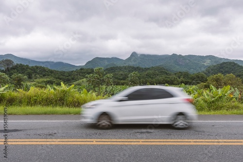 Driving along the highway in the rainforest. White hatchback car.