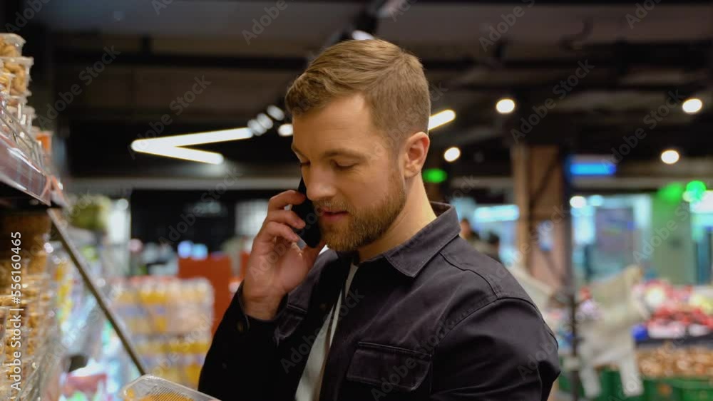 Portrait of young man doing grocery shopping in supermarket: calling his wife asking what healthy snack of nuts and dried fruit to choose Portrait of young man doing grocery shopping in supermarket: calling his wife asking what healthy snack of nuts and dried fruit to choose