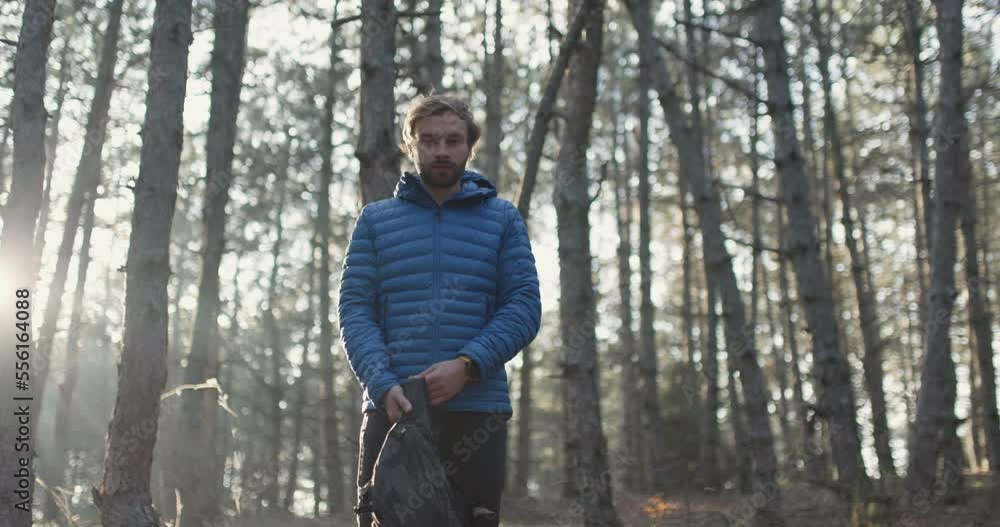 Portrait of a trail runner man standing in the woods. Putting on backpack. Sun shining through trees in a forest on sunset. Slowmotion video. Portrait of a trail runner man standing in the woods. Putting on backpack. Sun shining through trees in a forest on sunset. Slowmotion video.
