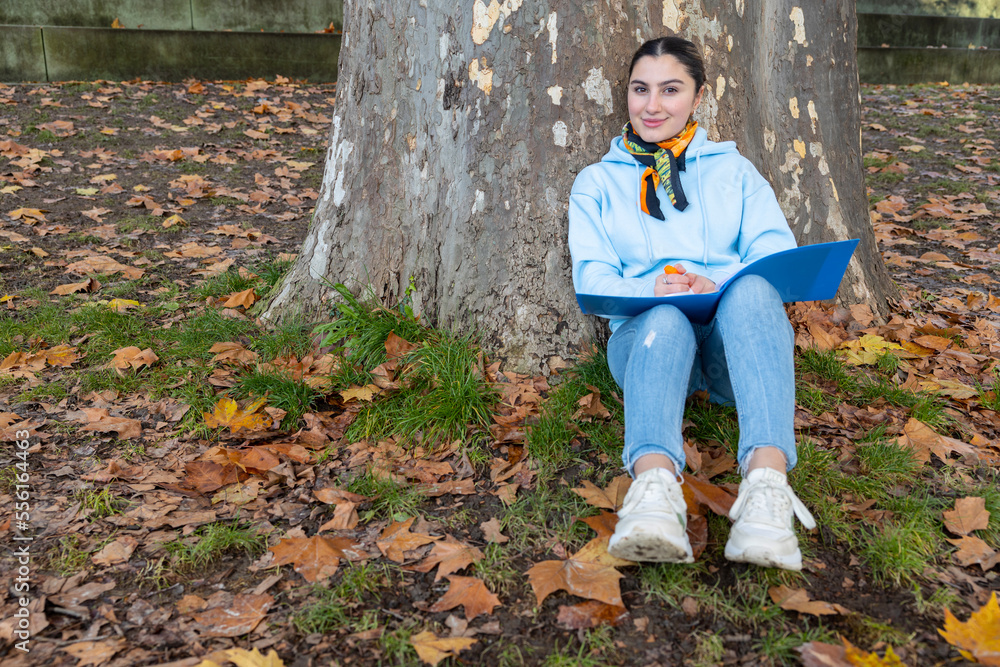 Oriental girl sitting under a tree with a blue folder in her hands, Austria Oriental girl sitting under a tree with a blue folder in her hands, Austria
