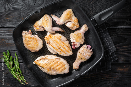 Roasted on a grill skillet chicken meat and chicken parts - drumstick, breast fillet, wing, thigh. Black wooden background. Top view