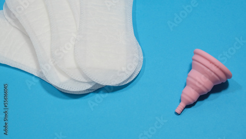Copa menstrual rosa plegable y compresas desechables en un fondo azul. Transición a la menstruación sostenible