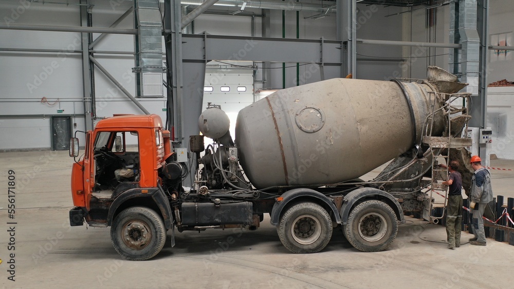 Pouring concrete mortar from a concrete mixer inside a huge production hangar. Filling the construction pit with cement mortar. Gray concrete mixer with orange cab.