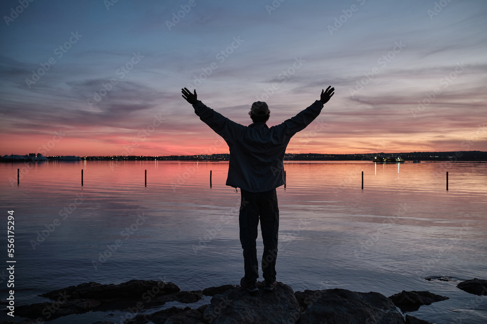 Person from behind looks at beautiful lake at sunrise. Relaxed, peaceful, thoughtful, happy and free at the lake.
Silhouette of a man standing by the lake and looking at the sunset.