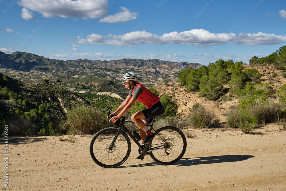 Obraz premium woman cyclist riding a gravel bicycle on the road in hills with mountain view, Alicante region in Spain 