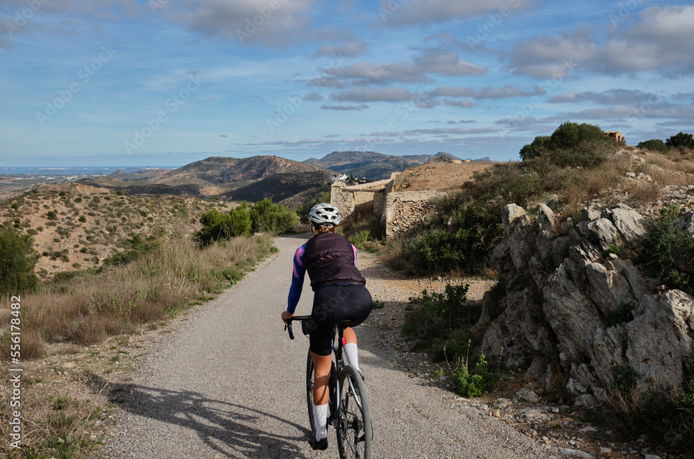 female cyclist riding a gravel bike on a gravel road with a view of the mountains, Alicante region of Spain