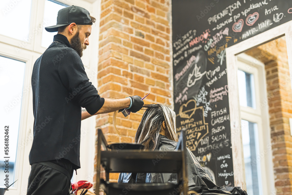Hairdresser in the black clothes with beard wearing black gloves dyeing his client's long hair in the professional hair salon. High quality photo Hairdresser in the black clothes with beard wearing black gloves dyeing his client's long hair in the professional hair salon. High quality photo