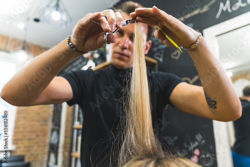 Focused professional male hairdresser cutting his female client's blonde hair with scissors in the professional hair salon. High quality photo photo