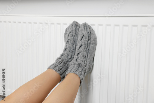 Woman warming legs on heating radiator near white wall, closeup