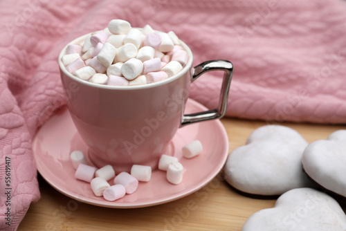 Cup of tasty cocoa with marshmallows, pink sweater and cookies on wooden table