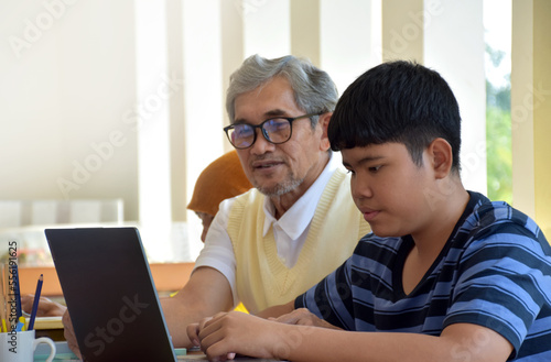 Asian boys are sitting infront of asian elderly teacher inside the room to ask and to do the school project work and listening to the elderly teacher about their project work, soft and selective focus