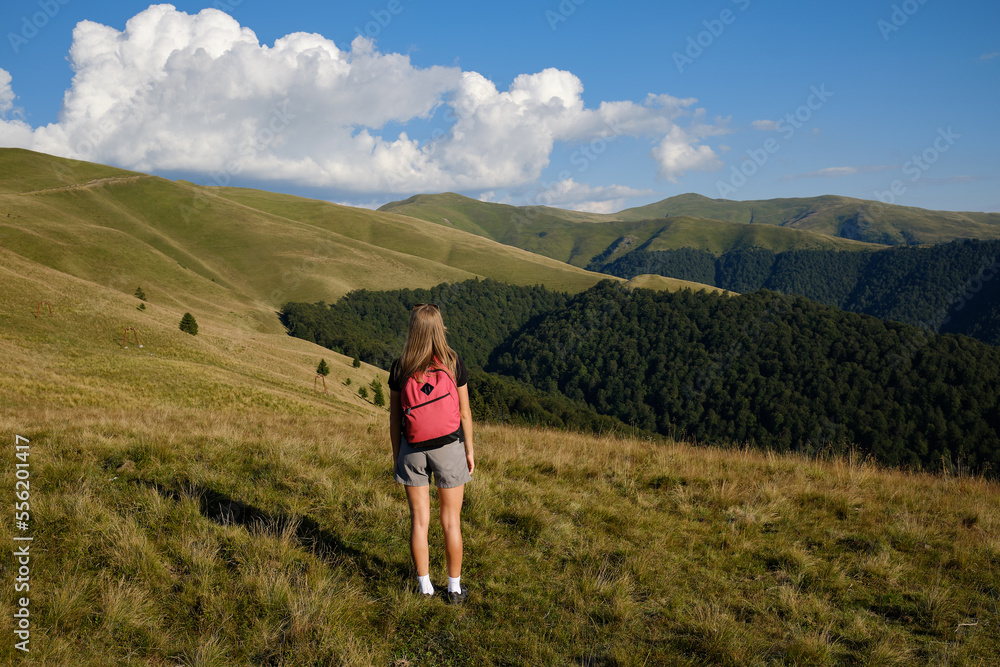 The girl stands on the edge of a high mountain . The girl looks at the beautiful mountain landscape