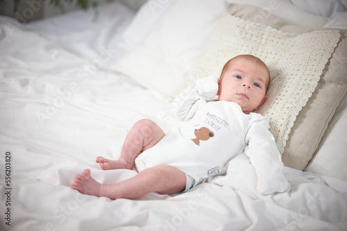 A charming boy in a white sunny bedroom. A newborn baby is resting in bed. Nursery for small children. Textiles and bed linen for children. Family morning at home.