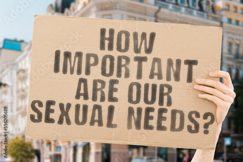 The question " How Important Are Our Sexual Needs? " is on a banner in men's hands with blurred background. Emotion. Conduct. Curious. Prostate. Date. Desire. Embrace. Enjoy. Enjoyment. Lovers