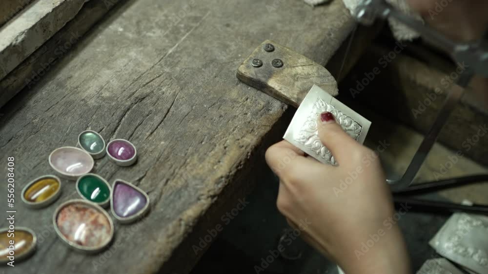 A craftsman is using tools to make silver jewelry. And there are gems as components. At the workbench. In the silver jewelry factory. in Nan province, Thailand A craftsman is using tools to make silver jewelry. And there are gems as components. At the workbench. In the silver jewelry factory. in Nan province, Thailand
