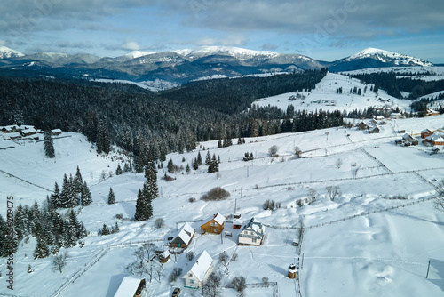 Winter landscape with small rural houses in remote settlement between snow covered forest in cold mountains