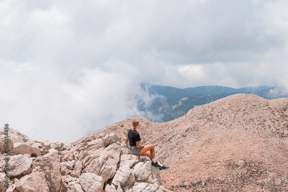 The girl is sitting on the edge of a high mountain in the clouds. The girl looks at the beautiful mountain landscape of Antalya, Turkey
