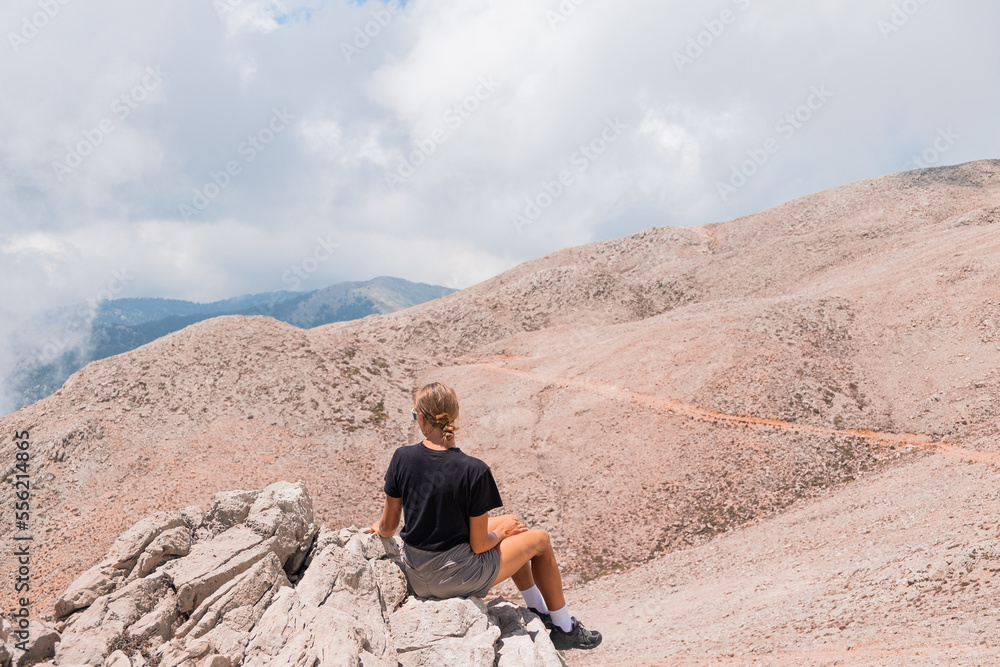 The girl is sitting on the edge of a high mountain in the clouds. The girl looks at the beautiful mountain landscape of Antalya, Turkey The girl is sitting on the edge of a high mountain in the clouds. The girl looks at the beautiful mountain landscape of Antalya, Turkey