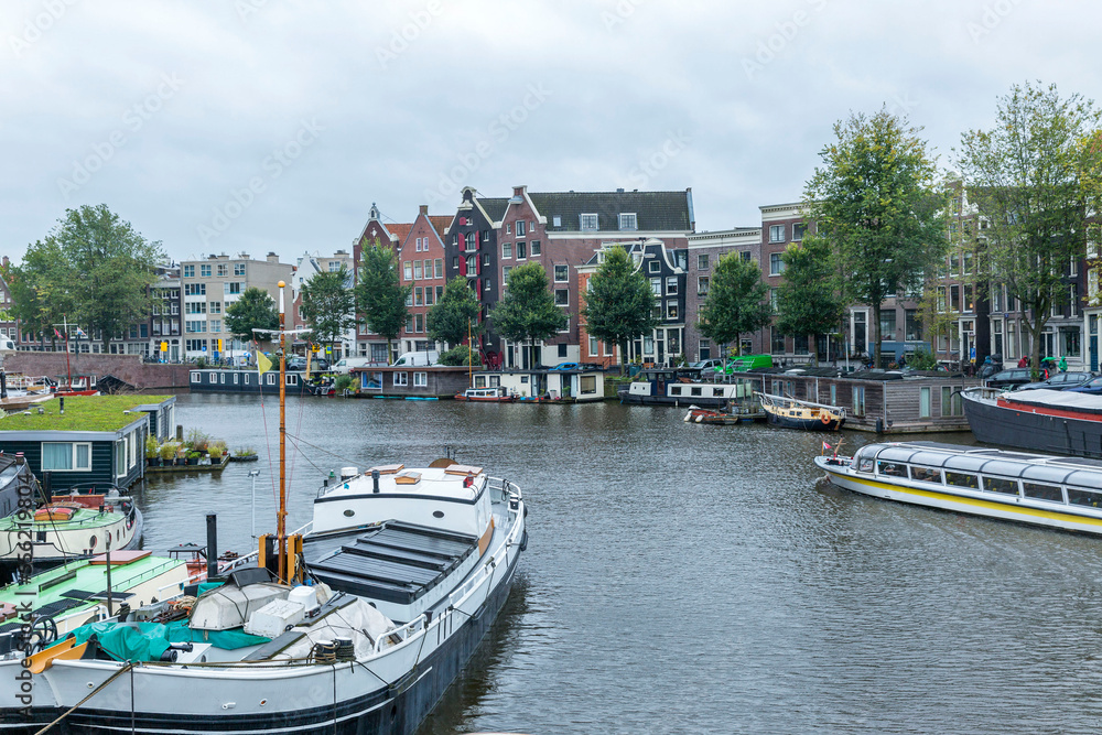 Boats and houses on a canal in Amsterdam. Beautiful landscape on a cloudy day. Tourism and travel.