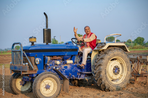 Indian senior farmer sitting on tractor at agriculture field.