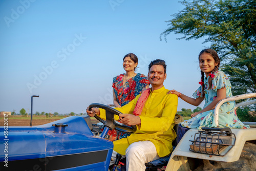 Indian farmer sitting on tractor with wife and little daughter. Indian rural family. © Niks Ads