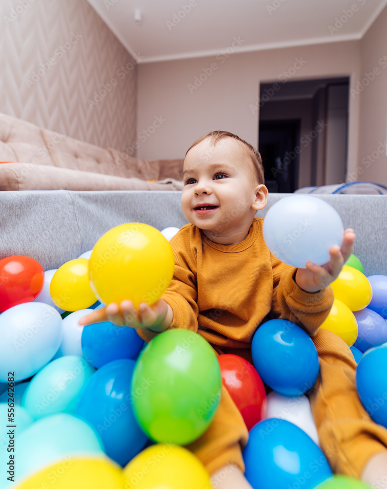 Cute little infant playing with colorful balls in dry pool. Little cute baby having fun in ball pit on birthday party at home. Cute little infant playing with colorful balls in dry pool. Little cute baby having fun in ball pit on birthday party at home.