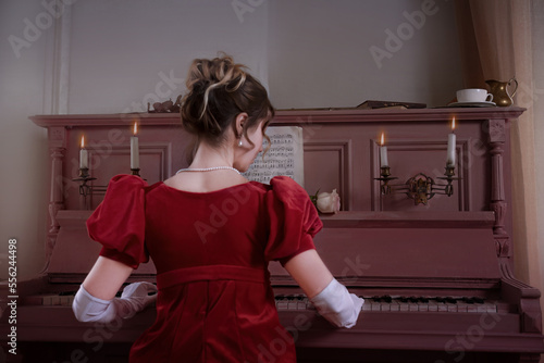 Young girl in a red vintage dress from the 19th century plays the piano photo