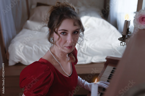 Young girl in a red vintage dress from the 19th century plays the piano