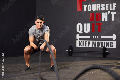 athletic young man doing exercises with battle rope in the gym