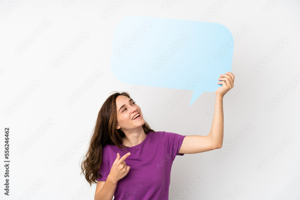 Young caucasian woman isolated on white background holding an empty speech bubble and pointing it Young caucasian woman isolated on white background holding an empty speech bubble and pointing it