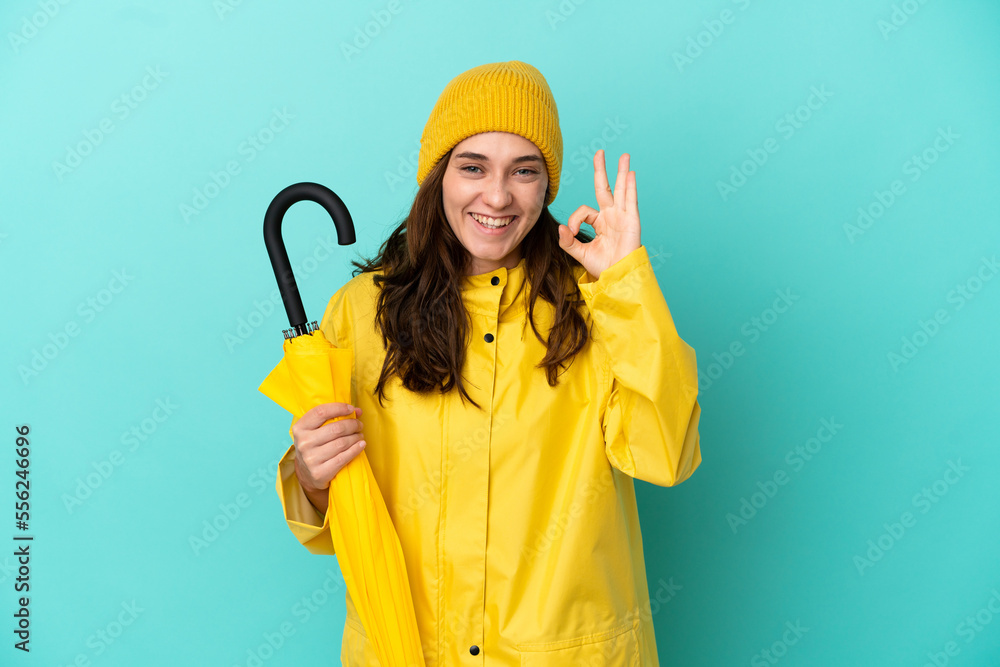 Young caucasian man holding an umbrella isolated on blue background showing ok sign with fingers