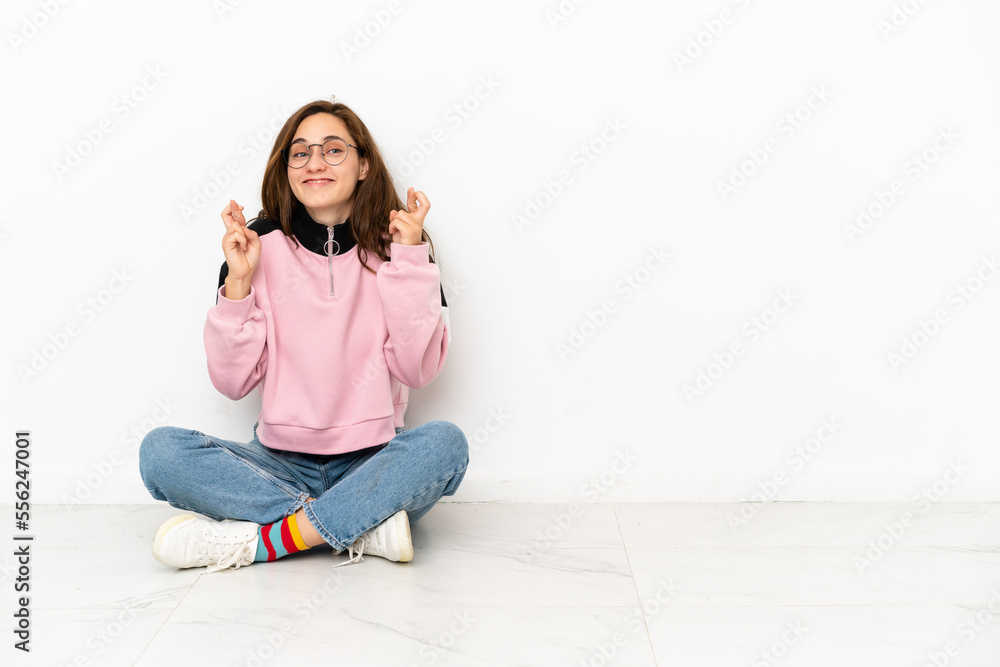 Young caucasian woman sitting on the floor isolated on white background with fingers crossing Young caucasian woman sitting on the floor isolated on white background with fingers crossing