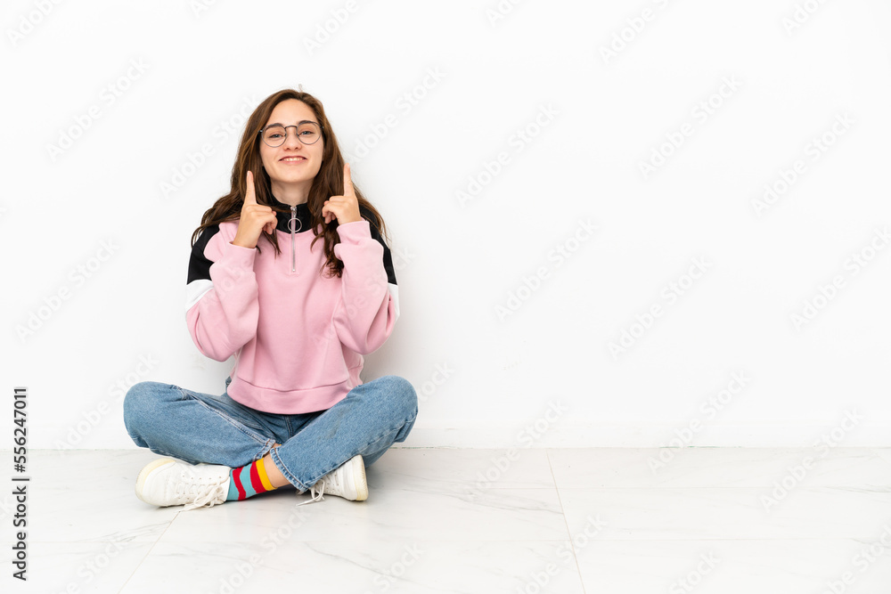 Young caucasian woman sitting on the floor isolated on white background smiling with a happy and pleasant expression Young caucasian woman sitting on the floor isolated on white background smiling with a happy and pleasant expression
