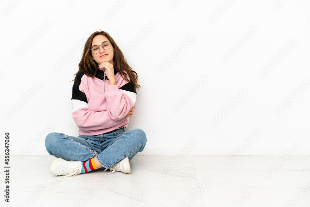 Young caucasian woman sitting on the floor isolated on white background with glasses and smiling