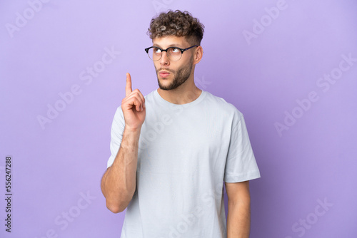 Delivery caucasian man isolated on purple background thinking an idea pointing the finger up