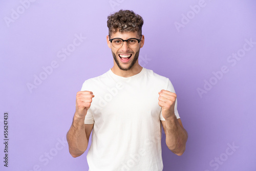 Delivery caucasian man isolated on purple background celebrating a victory in winner position © luismolinero