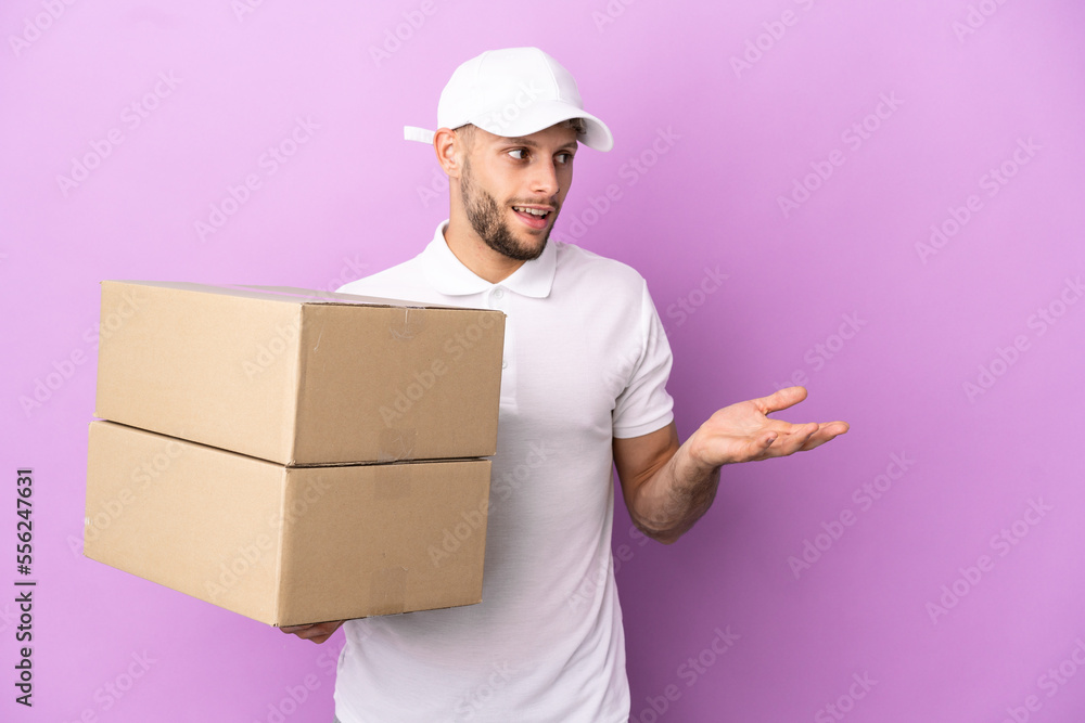 Delivery caucasian man isolated on purple background with surprise expression while looking side Delivery caucasian man isolated on purple background with surprise expression while looking side