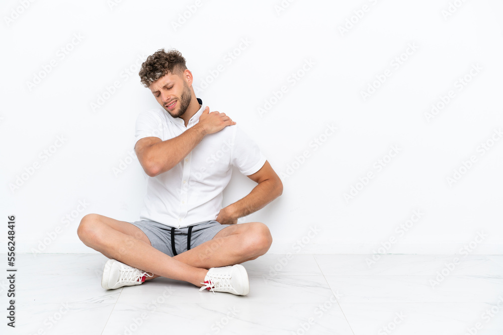 Fototapeta premium Young blonde man sitting on the floor isolated on white background suffering from pain in shoulder for having made an effort