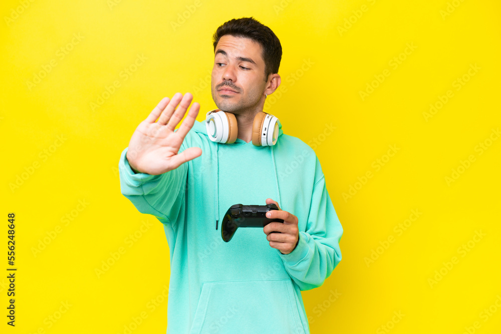 Young handsome man playing with a video game controller over isolated wall making stop gesture and disappointed Young handsome man playing with a video game controller over isolated wall making stop gesture and disappointed