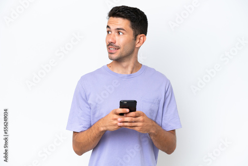 Young handsome man over isolated white background using mobile phone and looking up © luismolinero