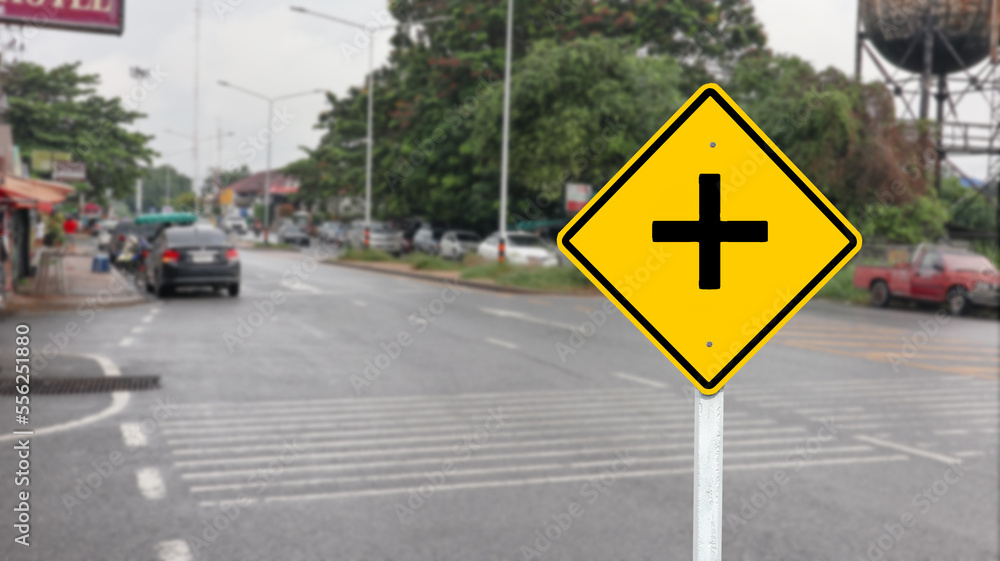 Yellow warn sign to beware of junction on blur background                          