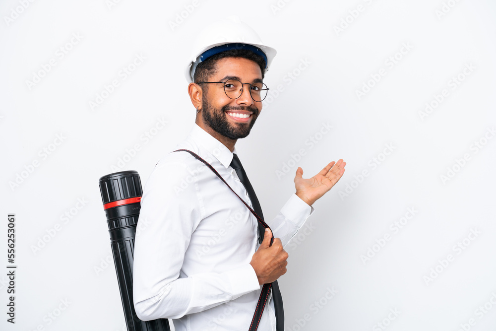 Young architect Brazilian man with helmet and holding blueprints isolated on white background extending hands to the side for inviting to come Young architect Brazilian man with helmet and holding blueprints isolated on white background extending hands to the side for inviting to come