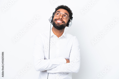 Telemarketer Brazilian man working with a headset isolated on white background looking up while smiling