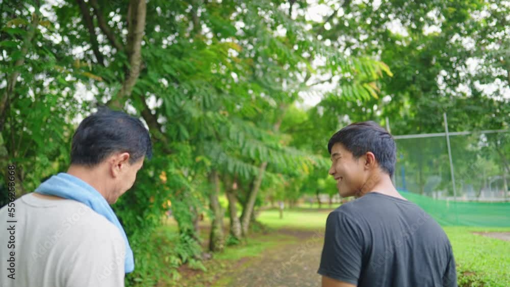 Warm Happy Dad and Adult Son having a quality time while jogging together in green park. Family Relationship and Bonds. Outdoors Recreational Activity. Cheerful middle aged father hugs his son. Warm Happy Dad and Adult Son having a quality time while jogging together in green park. Family Relationship and Bonds. Outdoors Recreational Activity. Cheerful middle aged father hugs his son.