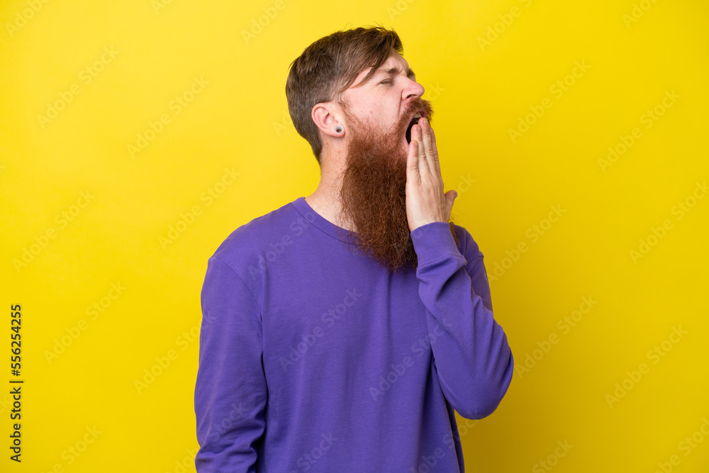 Redhead man with beard isolated on yellow background yawning and covering wide open mouth with hand Redhead man with beard isolated on yellow background yawning and covering wide open mouth with hand