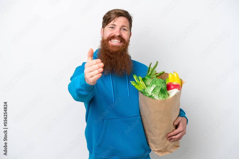 Redhead man with beard holding a grocery shopping bag isolated on white background shaking hands for closing a good deal Redhead man with beard holding a grocery shopping bag isolated on white background shaking hands for closing a good deal